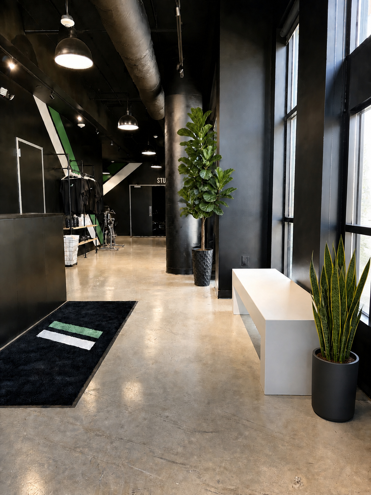 Rival Studios lobby and entry hallway with the black front desk, tall windows, a white bench, and potted plants